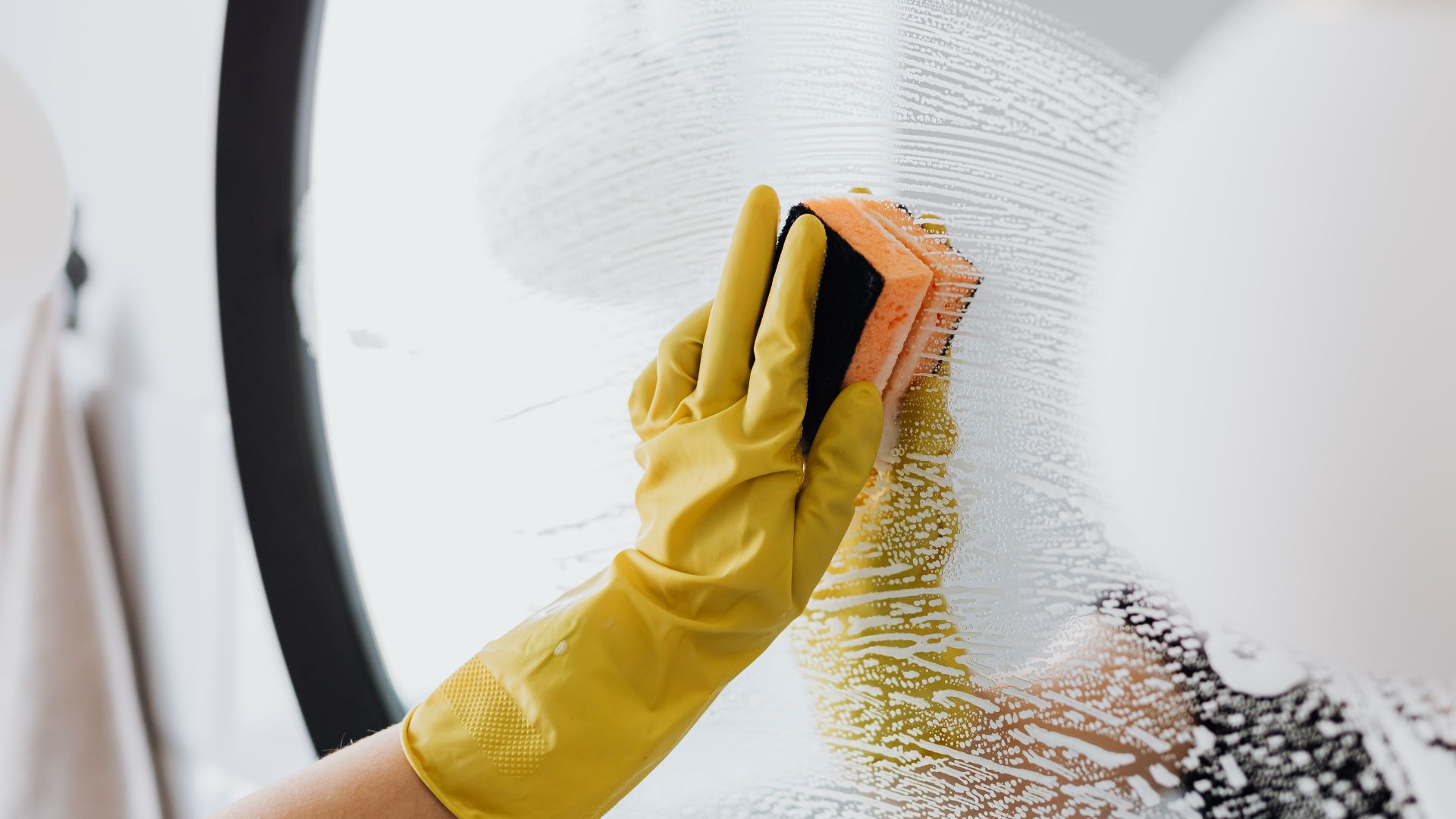 A person in yellow gloves and rubber gloves cleaning a wall